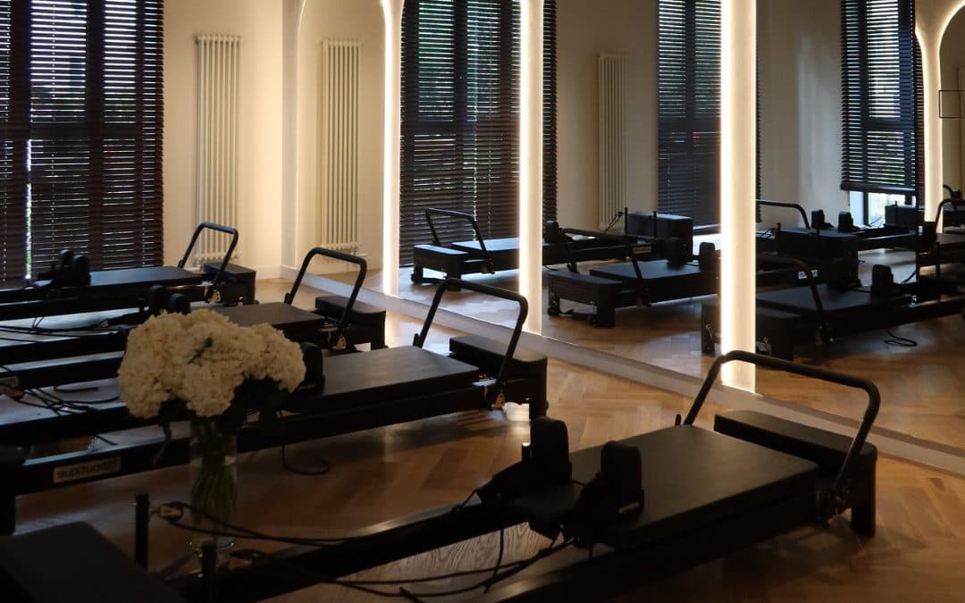 A row of FitBoutique Onyx Reformers in a studio with arched mirrors and timber floors